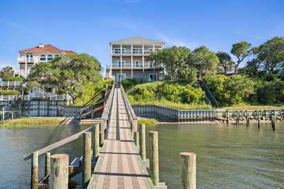 A private dock extends over calm waters, leading to a waterfront property nestled among coastal trees beneath a clear blue sky.
