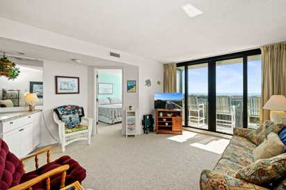 Relax in your spacious living room with comfortable seating, entertainment center, and stunning balcony views through floor-to-ceiling windows.