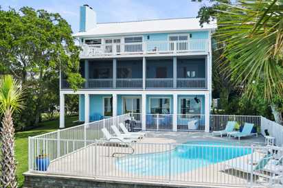 A charming coastal retreat with multiple levels of balconies overlooks a sparkling private pool surrounded by lush tropical palms and manicured lawns—perfect for sunny days and relaxed evenings.